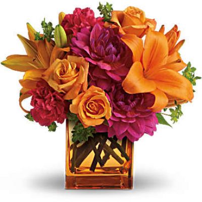 Feeling hot, hot, hot! This sizzling summer floral arrangement mixes hot pink dahlias and carnations with bright orange roses and lilies in an orange cube vase. It’s the floral equivalent of a trip to Miami in July!
Light orange roses, orange asiatic lilies, hot pink dahlias and hot pink carnations are presented with fresh green bupleurum in an orange glass cube vase.
