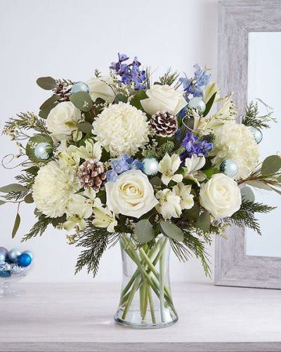 <p>Send wonderful winters wishes with our luxurious arrangement. Snowy white blooms are gathered with lush greenery, accents of blue, gray and glistening silver & gold. Loosely gathered in a glass vase, it’s a gift designed with stunning seasonal style.</p>